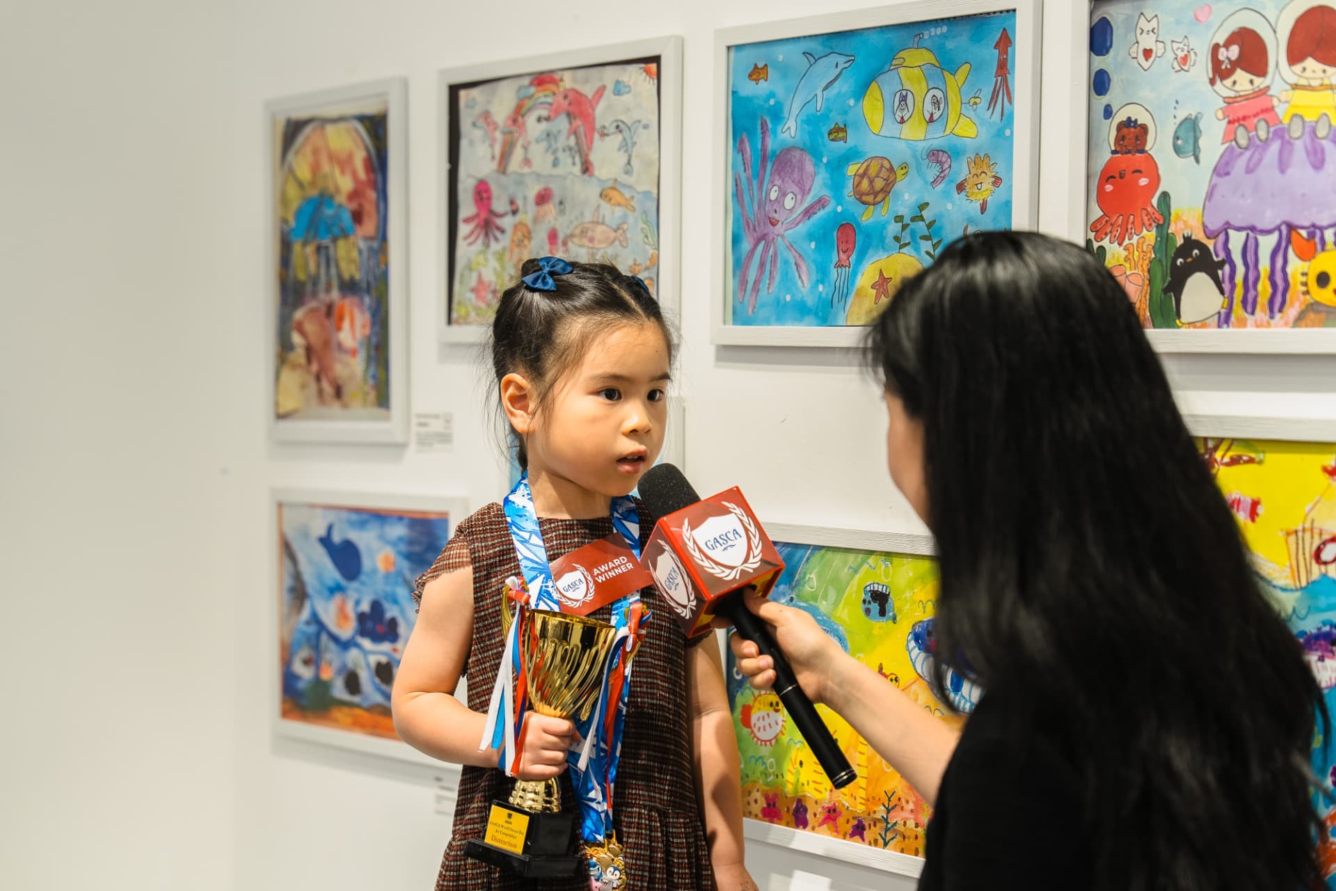 得獎小女孩手持獎盃於展覽場地接受訪問