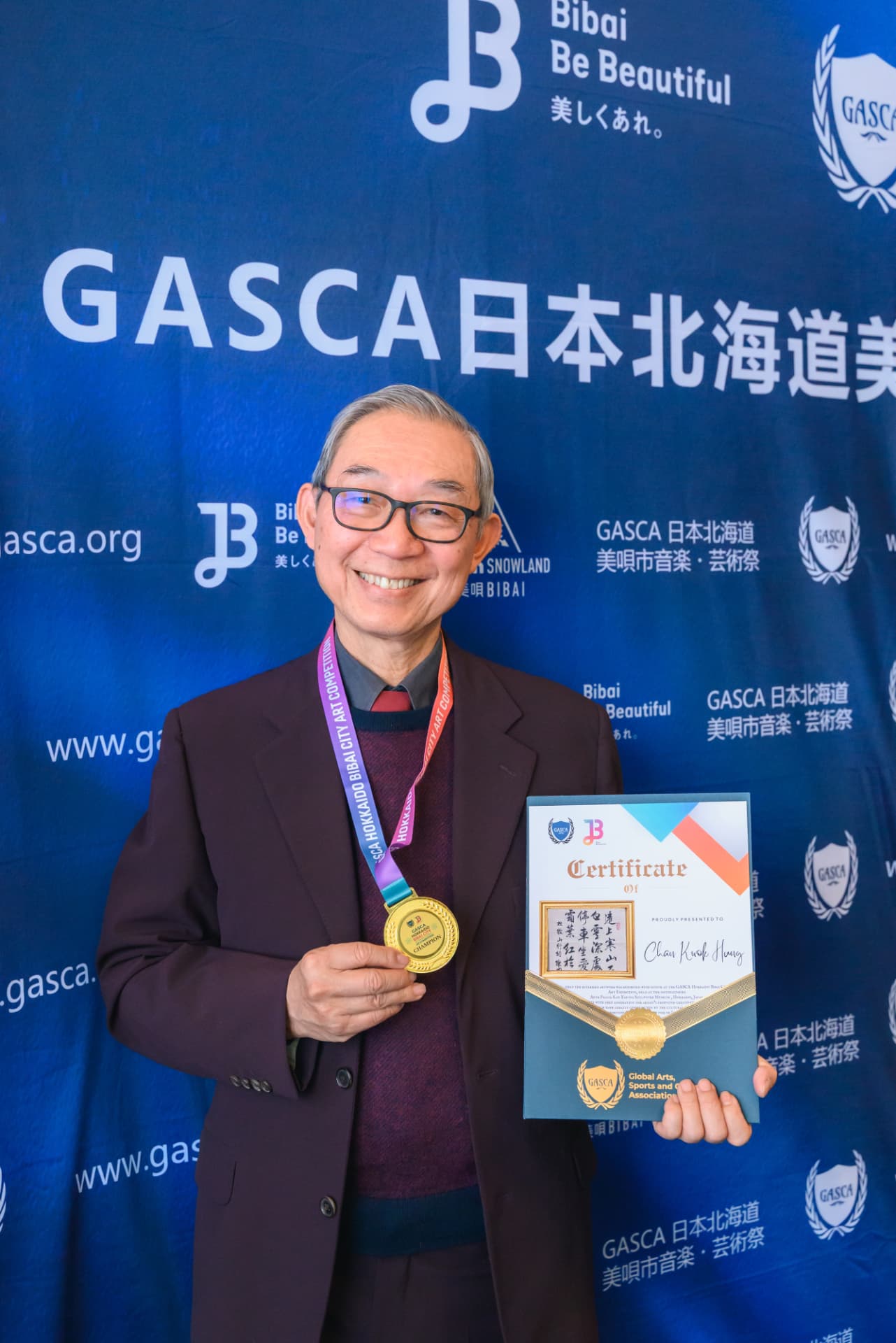 書法組冠軍得獎者手持金牌及證書於 GASCA 北海道美唄市背景板前留影
